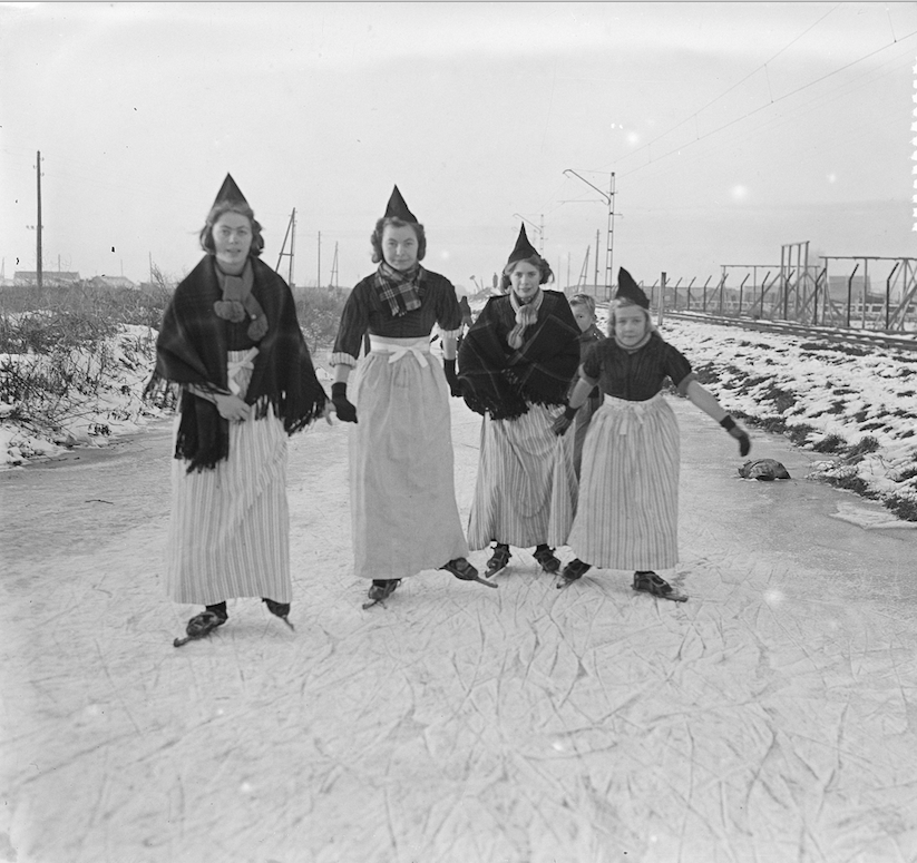 Links: Vier dames in klederdracht op het ijs, Volendam, 2 december 1952, gehuld in klederdracht. Rechts: het resultaat na inkleuren. (bron: Nationaal Archief, CCO, vervaardiger Harry Pot, Anefo)